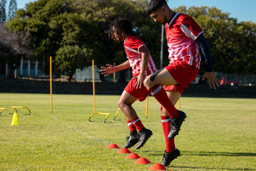 Obraz premium Side view of multiracial male players jumping on disc cones over grassy playground in summer