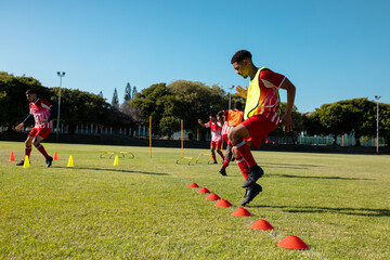 Fototapeta premium Male multiracial players running and jumping on grassy land at playground against clear sky