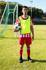 Portrait of young male player wearing uniform holding soccer ball in hand and standing in playground