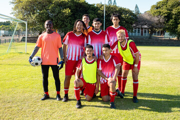 Portrait of cheerful male soccer team players in uniforms posing in playground during sunny day