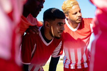 Multiracial male soccer athletes discussing while huddling in playground during match in summer