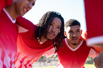 Multiracial male soccer athletes listening in meeting while huddling at playground during match