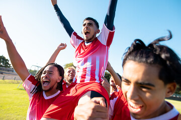 Multiracial male players carrying cheerful teammate on shoulders screaming while celebrating goal