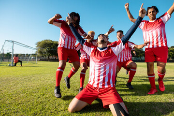 Multiracial team with arms raised running towards cheerful player screaming and kneeling on land