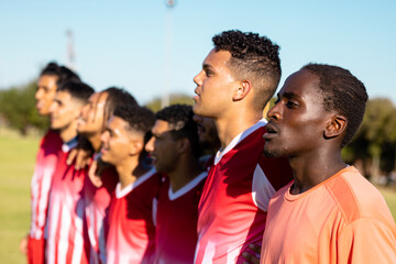 Multiracial male players in red uniforms looking away and standing side by side against clear sky