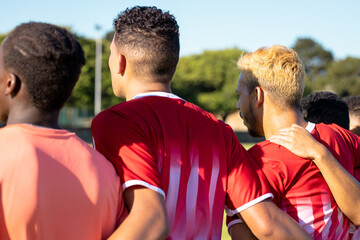 Rear view of multiracial male players in uniforms with arms around standing side by side