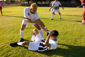 Caucasian player giving hand to injured teammate lying on field in getting up during match
