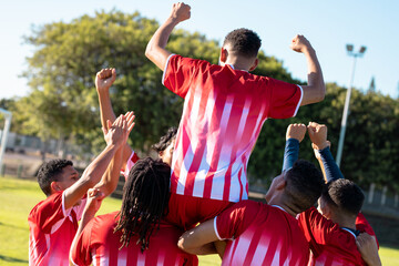 Rear view of multiracial cheerful players carrying teammate on shoulders while celebrating goal