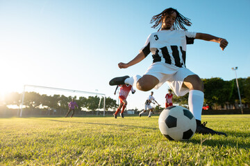 Low angle view of multiracial player kicking ball while playing soccer match against clear sky