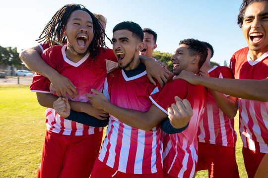 Multiracial male team players screaming while celebrating victory after soccer match at playground