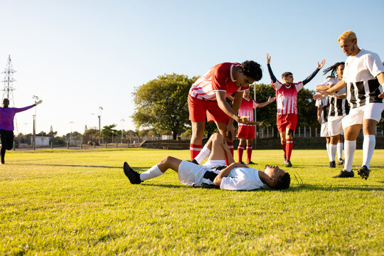 Multiracial male soccer teams running towards injured player lying on grassy field during match