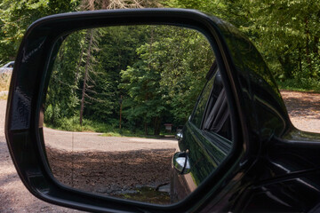 View of the road to the forest through the rearview mirror of the car. You can see dense vegetation...