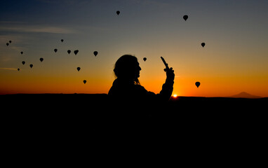 Silhouette of Smart phone in hands of woman taking pictures of a beautiful landscape and balloons in Cappadocia. Sunrise time, dreamy travel concept