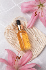 Unbranded serum bottle on cotton bag with lily flower on marble background. Beauty concept for face and body care