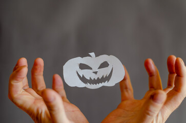 White Paper Halloween Pumpkin and hands with fingers bent in terror. Halloween paraphernalia cut with scissors from sheet of paper. Flying in ir Silhouette Smiling intimidating face. Man's hands