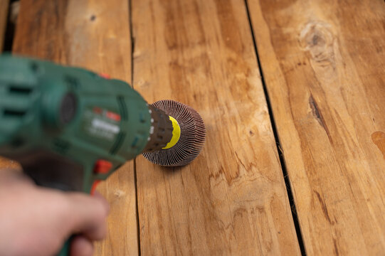 Man processes wooden boards with power tool. Flap wheel in the cam of the electric drill chuck. Tool for woodworking, sanding, removing rust from various surfaces. Indoors. Close-up. Selective focus