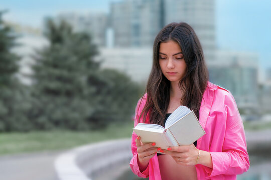 Gorgeous young brunette reading novel sitting with book in hands. Female reader outdoor.