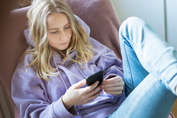 Teenage girl in purple hoodie text messaging on smart phone