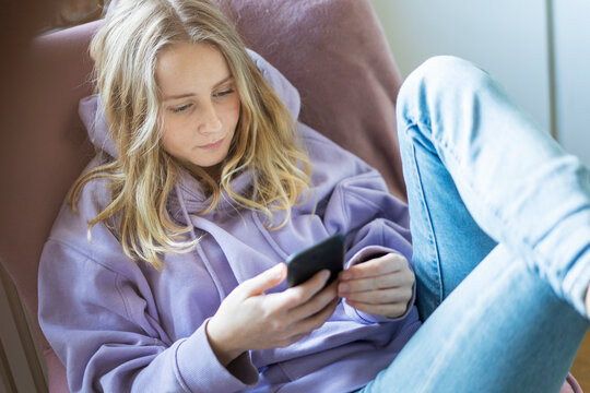 Teenage girl in purple hoodie text messaging on smart phone