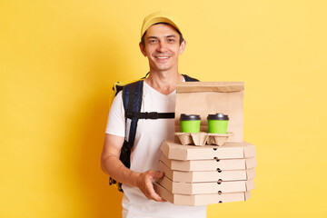 Image of satisfied man courier with thermo backpack in white T-shirt and cap isolated over yellow...