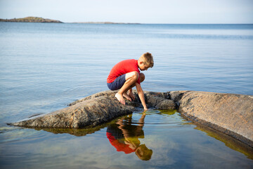 Boy crouching on rock in sea