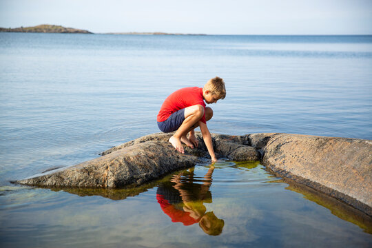 Boy crouching on rock in sea