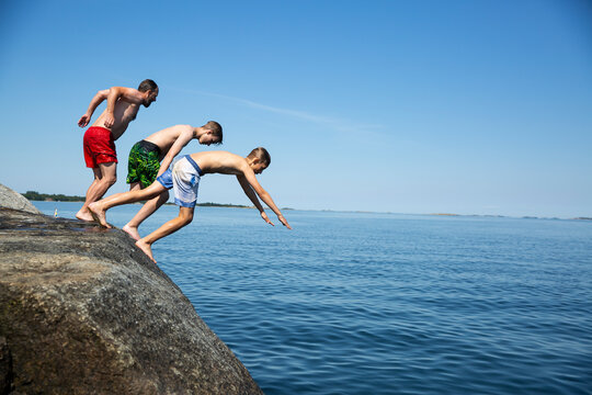Father and sons diving from rock into sea