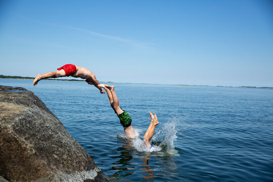 Father and sons diving from rock into sea