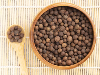 Spice Allspice (Jamaica pepper, Pimento) in wooden bowl and spoon on background of tied wooden sticks. Top view. Indian cuisine concept