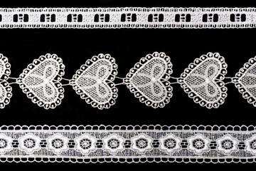 White lace with flowers and hearts and leaves isolated on black background horizontally