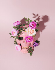 Pink human skull mask with floral arrangement on pastel pink background. Gothic style, death symbol, bizarre decoration. 