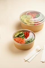 Trendy wholesome dish poke or buddha bowl - rice, wakame seaweed, tomatoes, cucumber, and red fish salmon - in a recycled round carton with sustainable fork, takeaway food concept on beige background