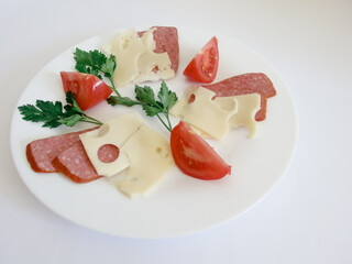 Still life. Sliced tomatoes, cheese sausage salami on a white plate. Light background.