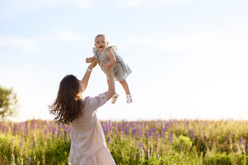 Beautiful young Caucasian mother with a little girl in her arms on the background of the sunset in a field of lupine flowers are hugging