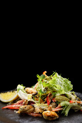 Salad with mussels, on a black plate. vertical
