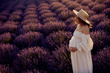 the pregnant girl with a hat in the lavender field on a sunset