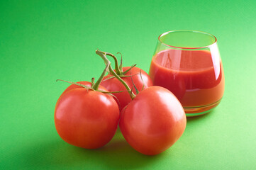 tomato juice in a glass glass and tomatoes on a branch on a green background