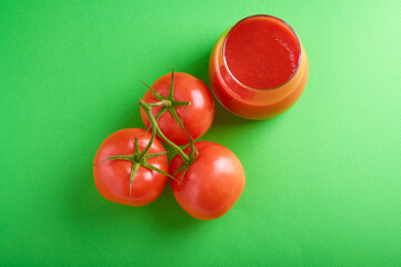 top view of tomato juice in a glass glass and tomatoes on a branch on a green background