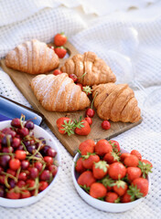 Strawberries on a plate on the background of a white blanket on a picnic in a green field with croissants