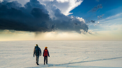The two people with backpacks walking through the huge snow field