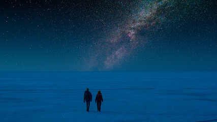 The two people walking through the snow field on the starry sky background