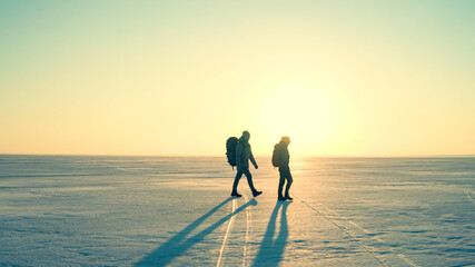 The two travelers with backpacks trekking through the snow field
