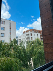 Close up of a window with rain drops with resident houses and trees in the background. Blurred background of mid sized residential apartments and water droplets in focus.