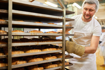 Bäcker schiebt Regalwagen mit fertig gebackenen Croissants