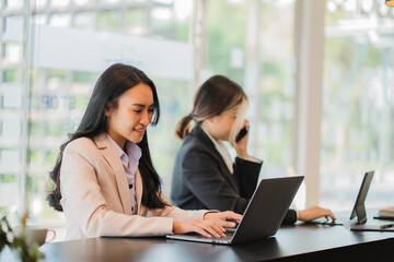 Two Asian female accountants working in the office with laptop computers and financial documents on the table.