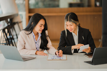 Two Asian female accountants working in the office with laptop computers and financial documents on the table.