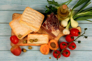 Soft French cheese, Spanish ham and vegetables on a kitchen wooden board. blue rustic wooden background