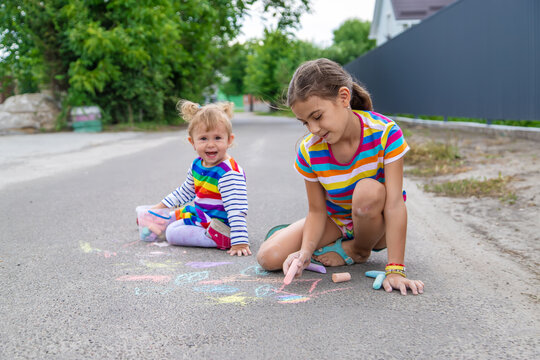 The child draws with chalk on the pavement. Selective focus.