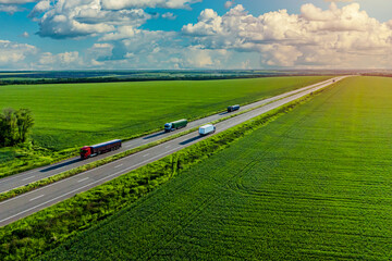 convoys with cargo. trucks on the higthway sunset. cargo delivery driving on asphalt road along the green fields. seen from the air. Aerial view landscape. drone photography.