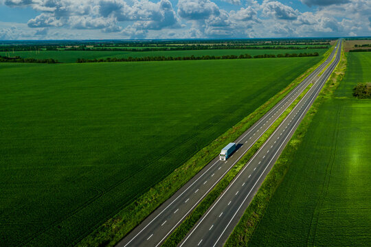 white truck driving on asphalt road along the green fields. seen from the air. Aerial view landscape. drone photography. cargo delivery and transportation concept